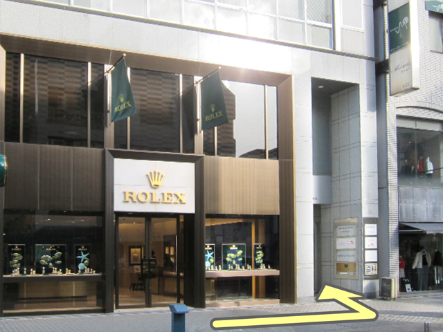ROLEXの入り口を過ぎたところにビルの入り口がございますので、お入りいただき奥のエレベーターの方へお進みください。